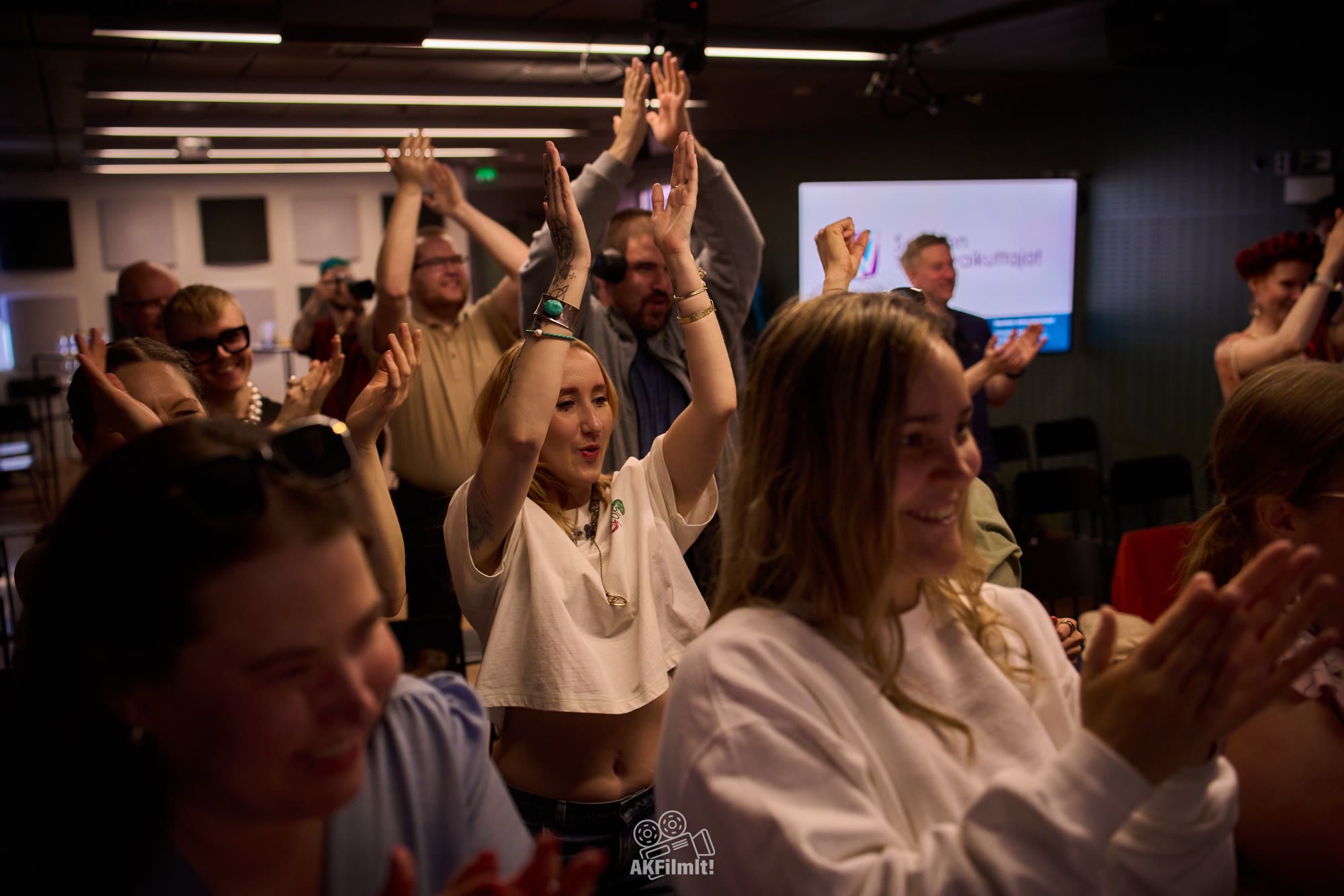 An audience on its feet, arms in the air, laughing and clapping