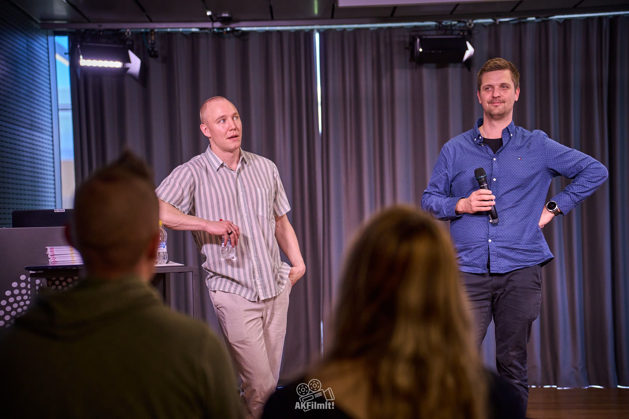 Ronny Eriksson in a striped shirt on a small stage, a second speaker beside him, audience in front