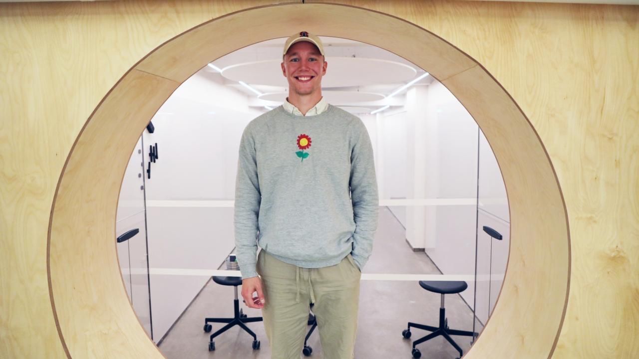 Ronny Eriksson standing in a round plywood portal, a red flower pinned to his sweater