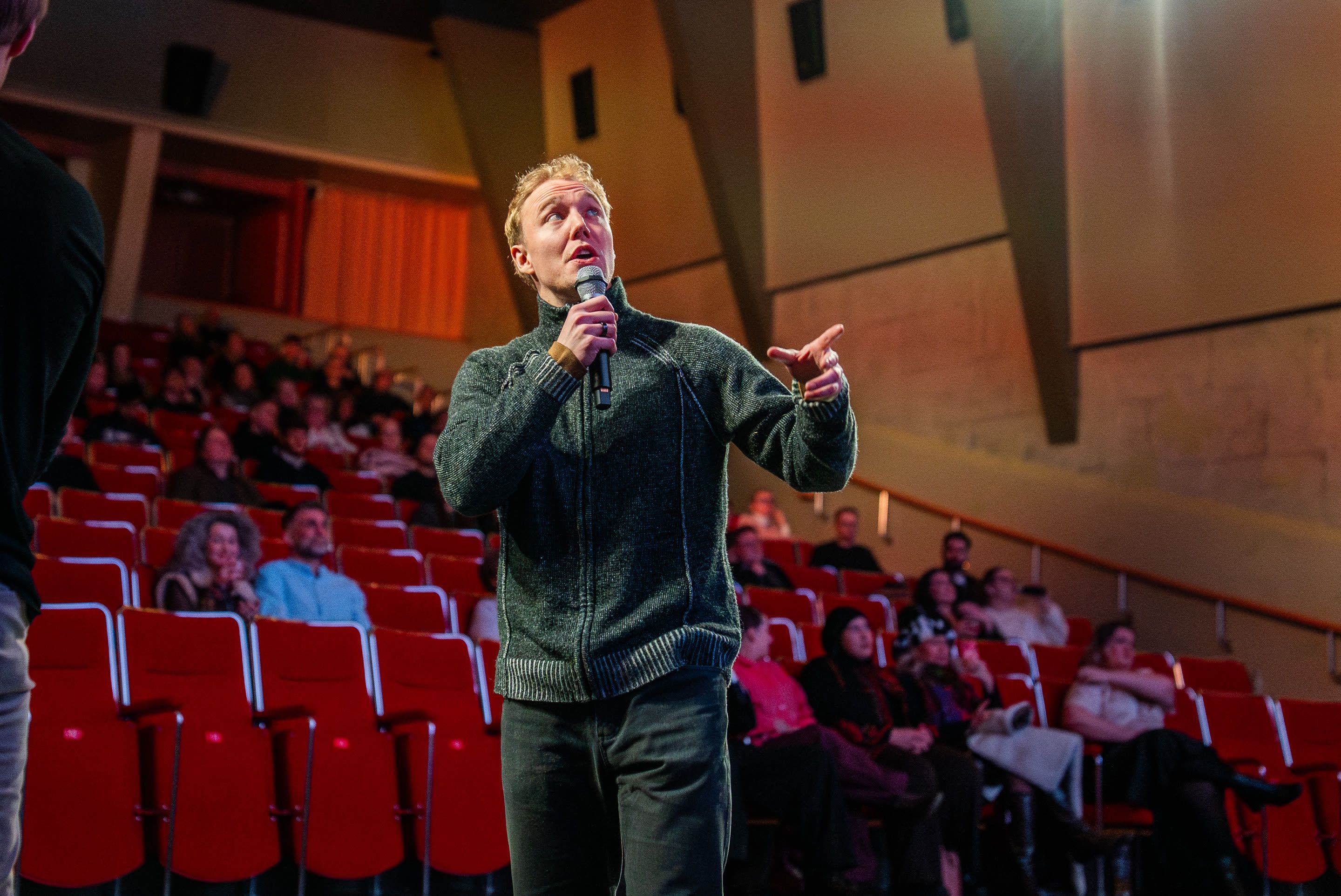 Ronny Eriksson, microphone in hand, mid-⁠sentence in the aisle of a cinema with red seats and a listening audience