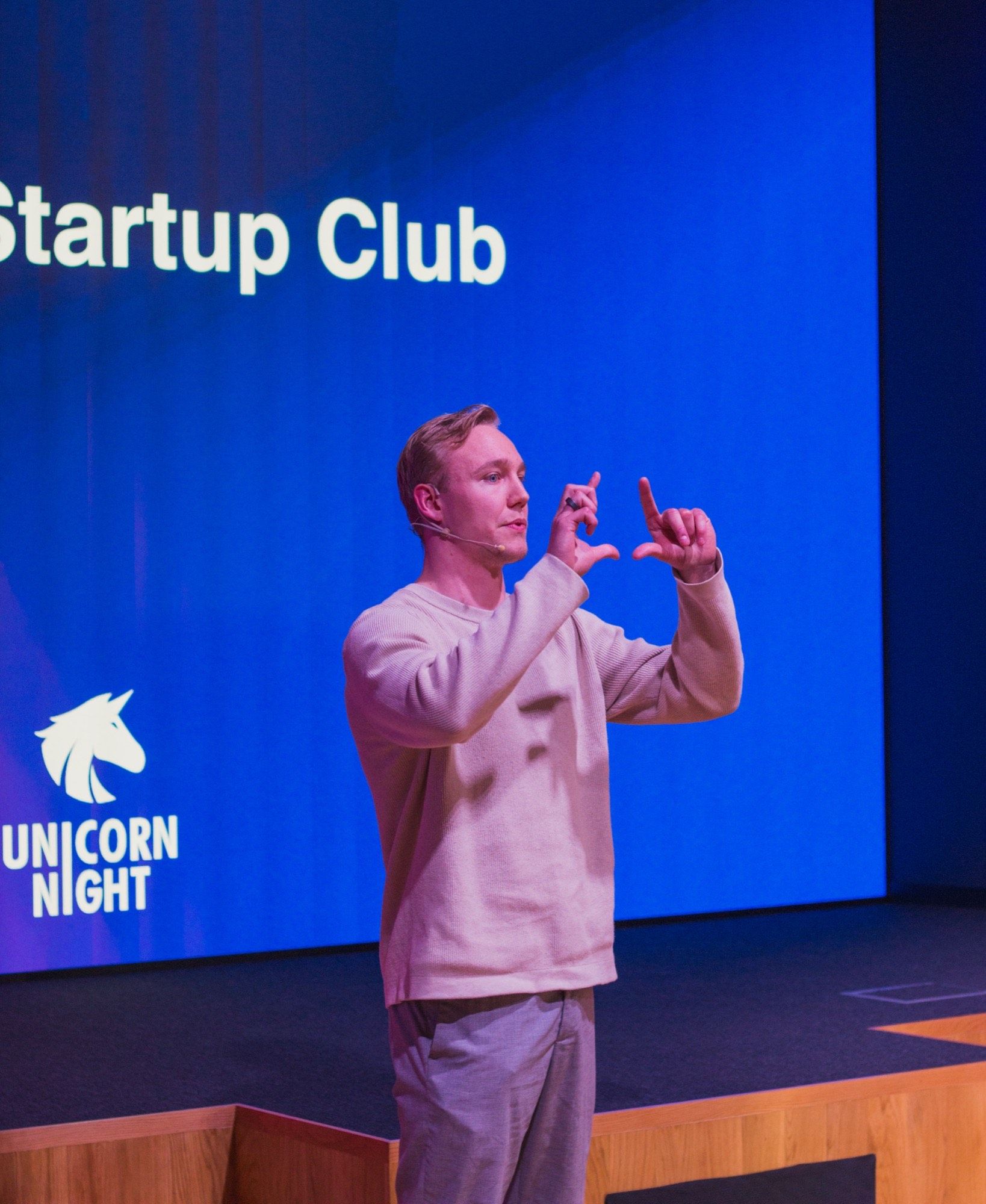 Ronny Eriksson with a headset microphone, framing the view with both hands, in front of a blue Unicorn Night screen