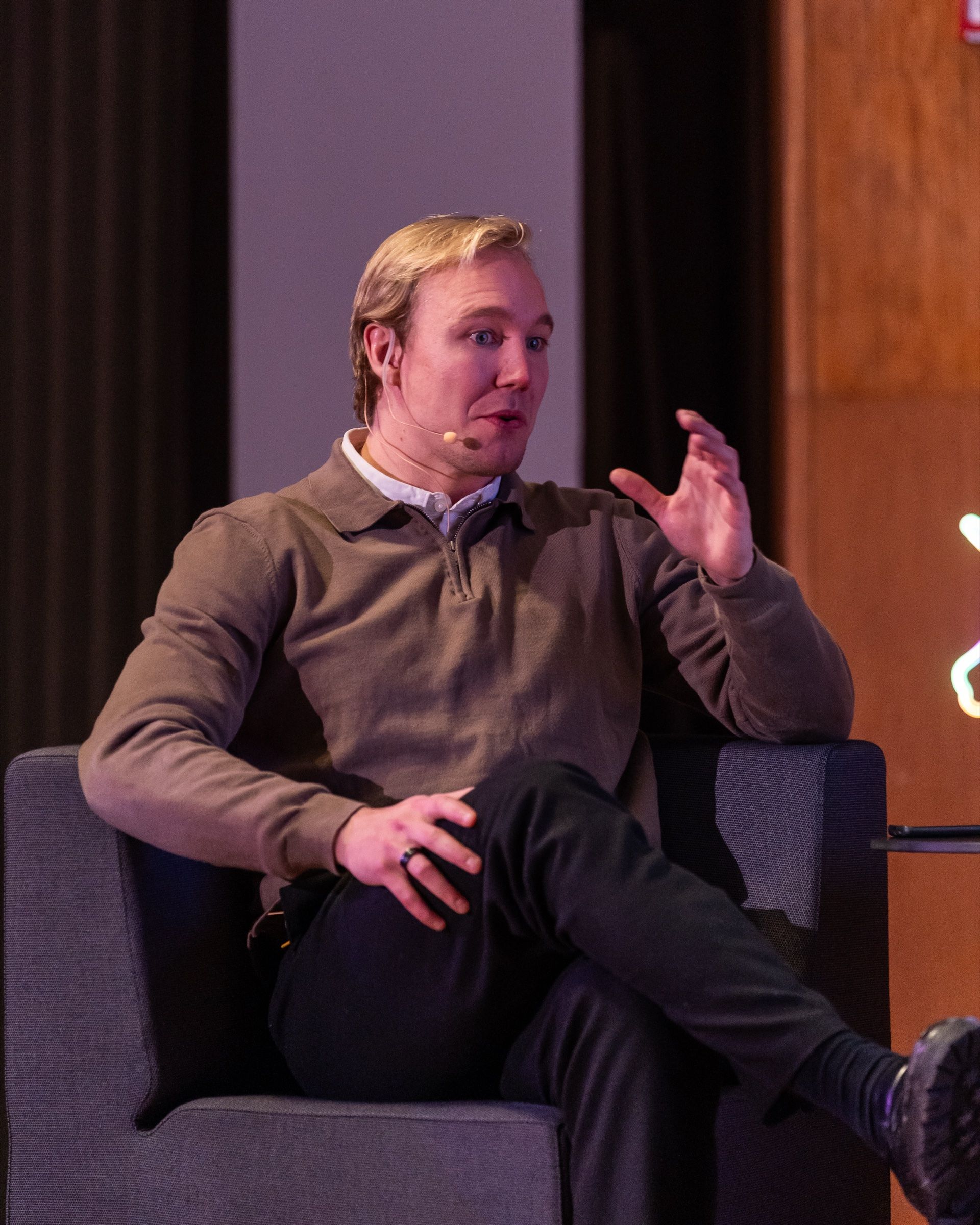 Ronny Eriksson in an armchair on stage, mid-⁠sentence, in a brown polo shirt