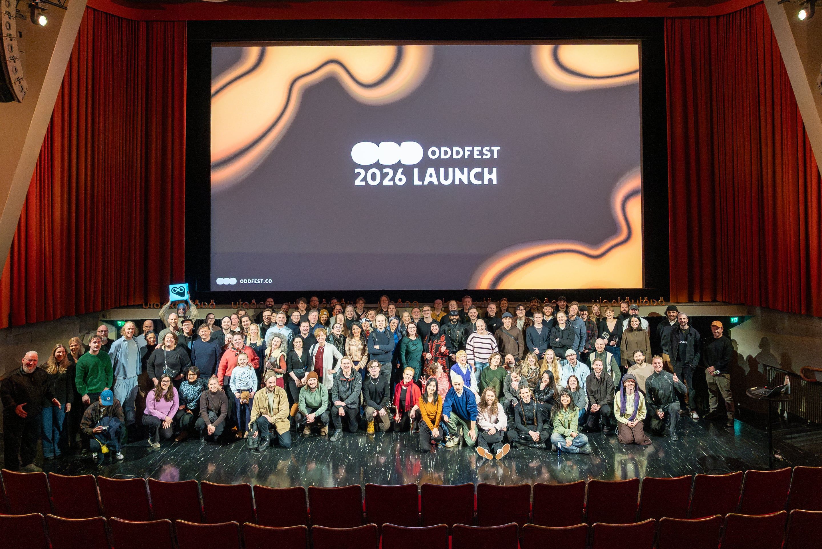 A large group gathered together on a cinema stage under a screen reading ODDfest 2026 launch