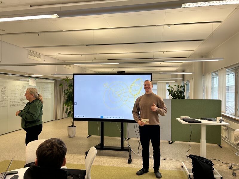 Participants at tables in a bright office, a map on the screen, Ronny Eriksson standing beside it