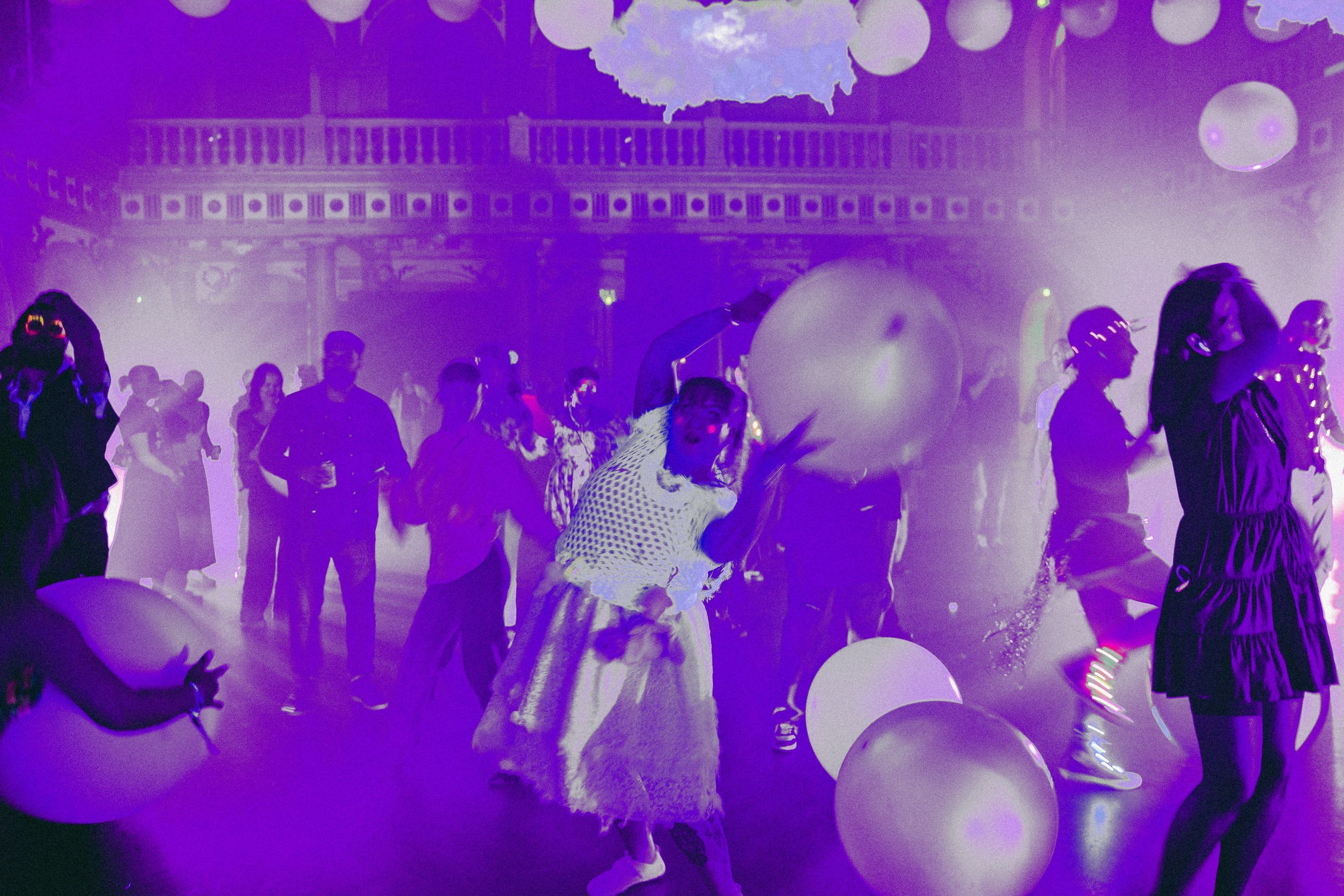 A packed hall at Vanha ylioppilastalo in violet light, dancers among dozens of large white balls, clouds hung under the balcony