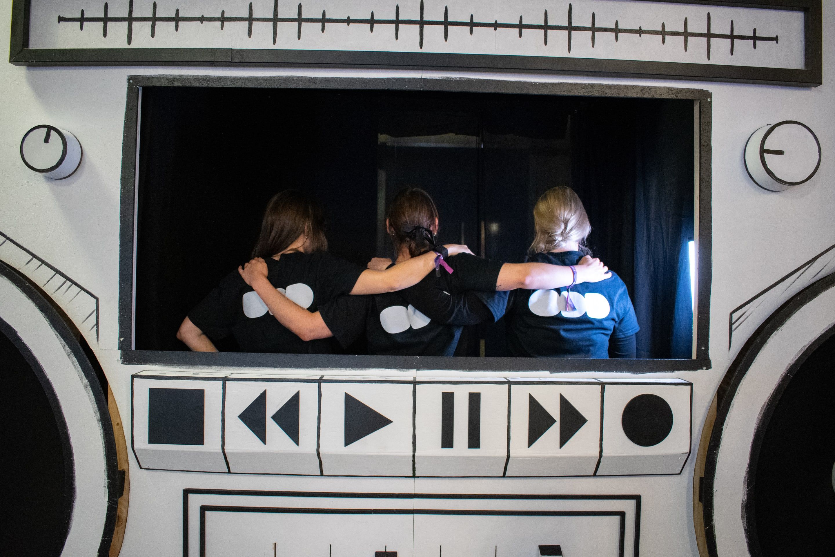 Three volunteers in ODD t-shirts, backs to the camera, arm in arm inside the window of a giant hand-painted boombox