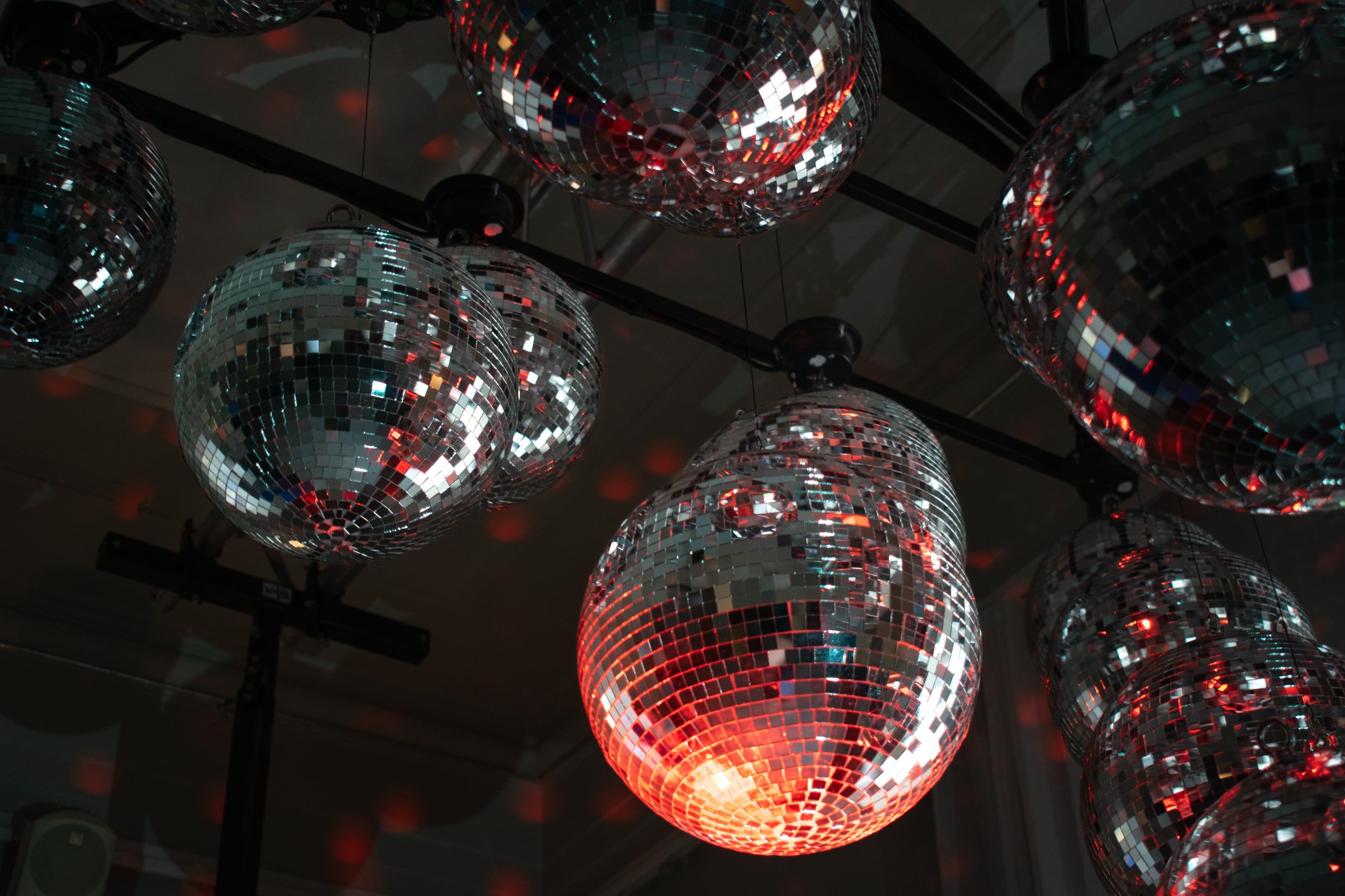 A cluster of mirror balls hanging under a dark ceiling, one lit orange