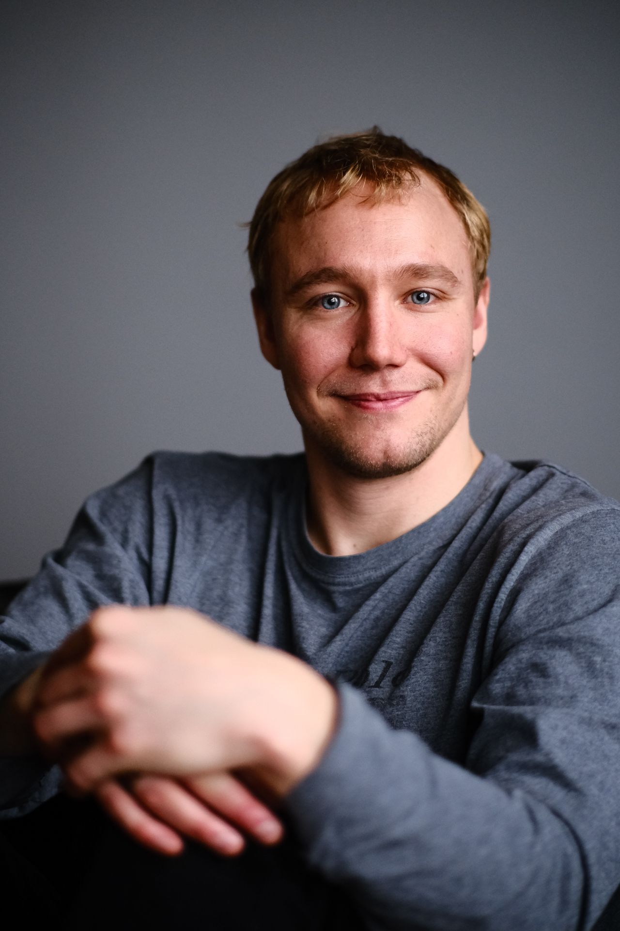 Ronny Eriksson in a grey long-sleeved top against a grey backdrop, forearms crossed in front of him, smiling at the camera